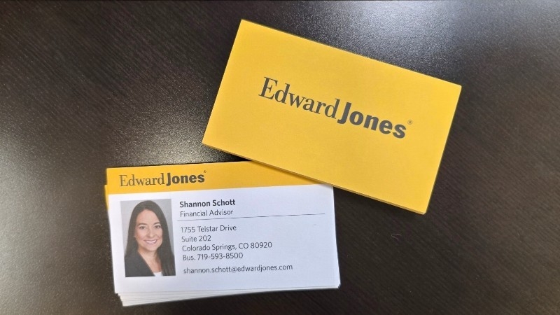 A stack of Edward Jones business cards on a dark desk, with one card showing contact details and a photo of a financial advisor named Shannon Schott.