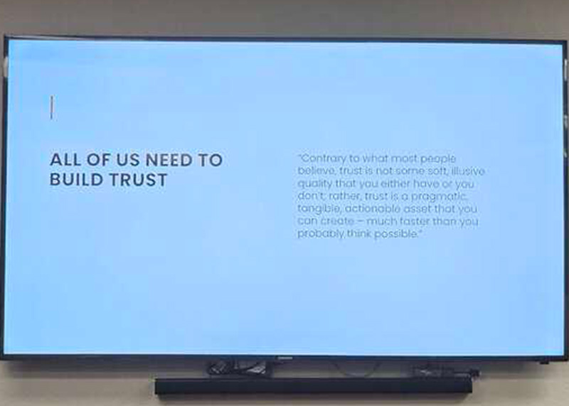 A presentation slide with the heading "All of us need to build trust" and a quote about trust as a pragmatic, actionable asset, displayed on a large screen.